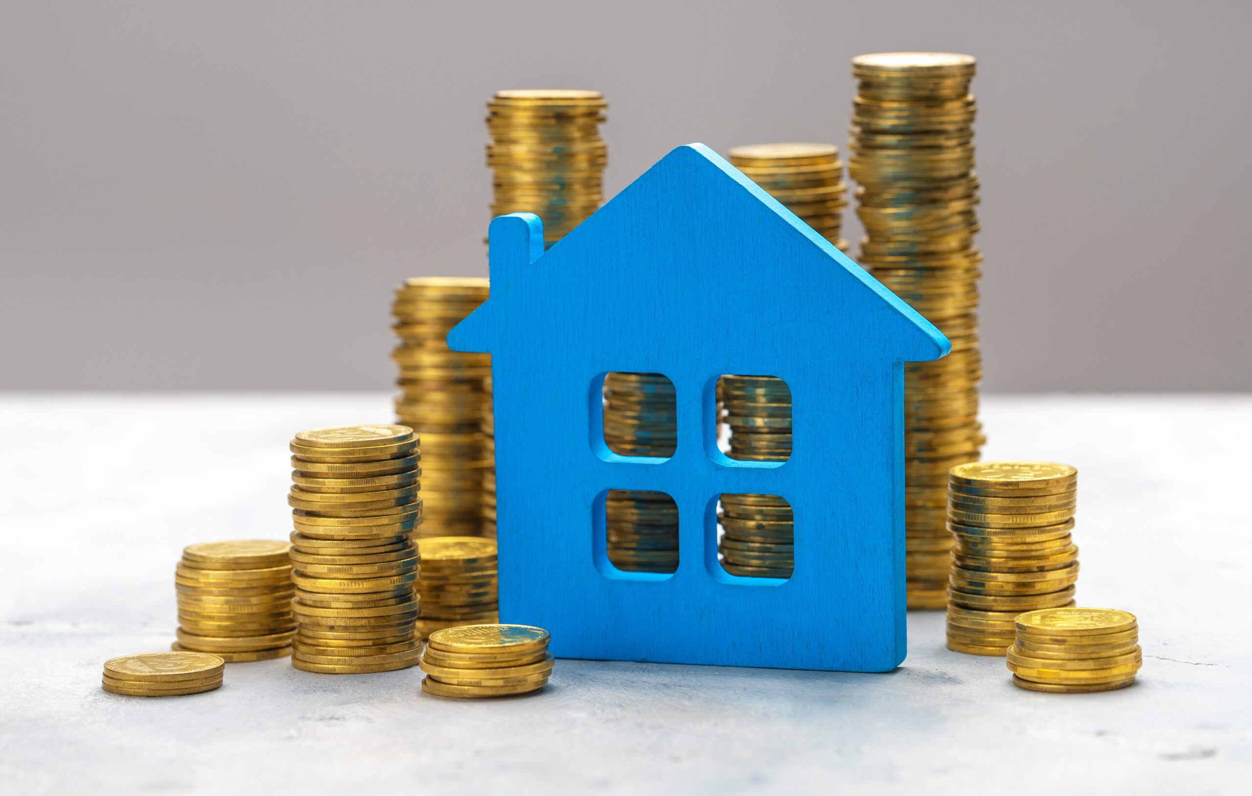 Expensive real estate. Blue house and stacks of gold coins on a