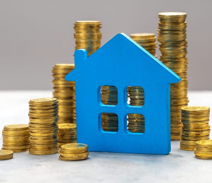Expensive real estate. Blue house and stacks of gold coins on a